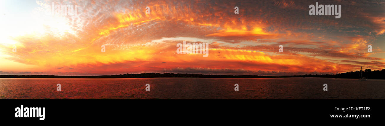 Eine markante inspirational gold und orange gefärbt bewölkter Sonnenuntergang Marine über Meer Wasser mit Wasser Reflexionen. am Lake Macquarie erfasst. Stockfoto