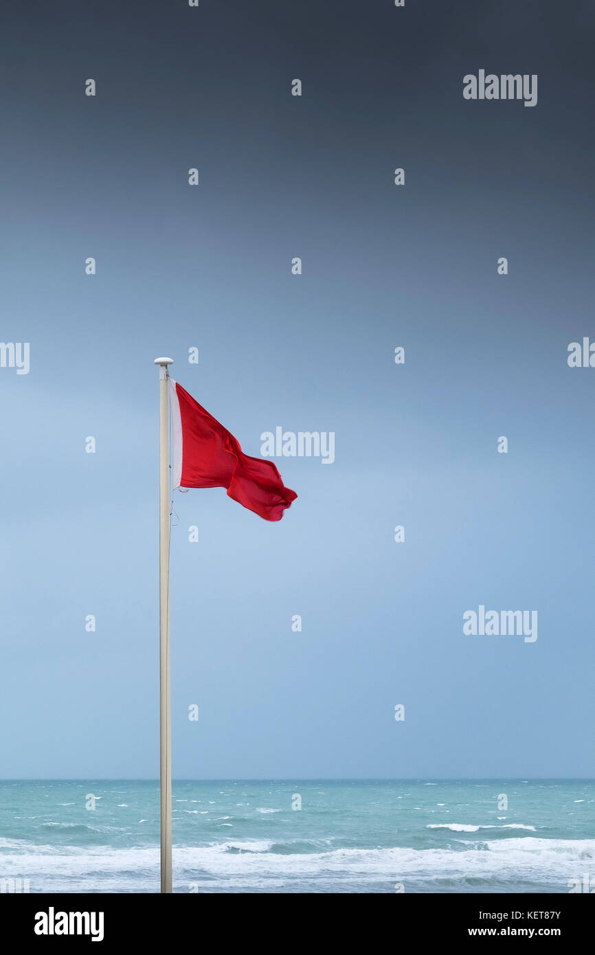 Rote Fahne - eine rote Flagge in High Wind am Fistral Beach Newquay Cornwall fliegen. Stockfoto