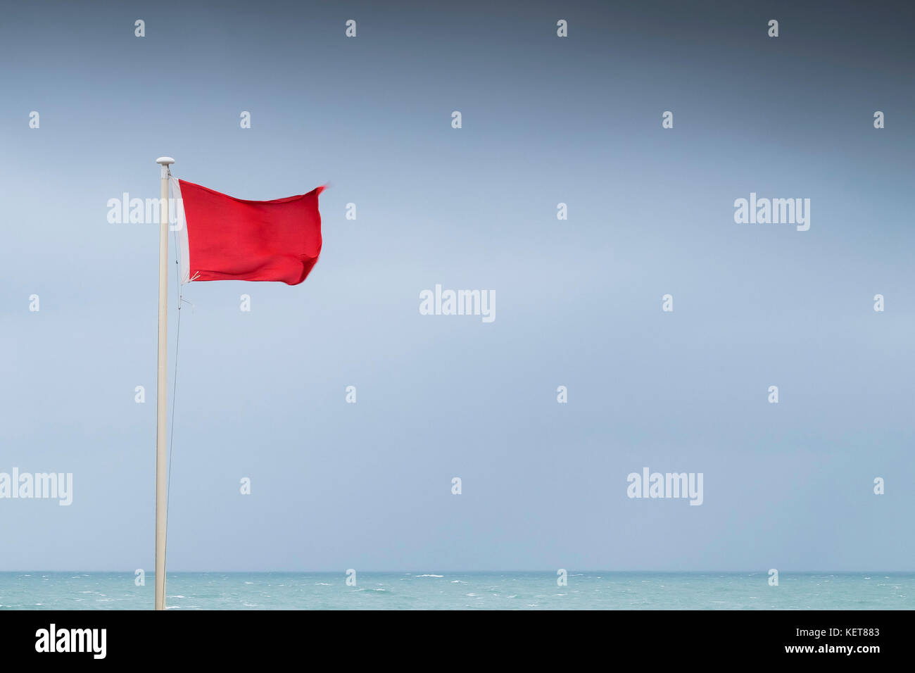 Rote Fahne - eine rote Flagge in High Wind am Fistral Beach Newquay Cornwall fliegen. Stockfoto