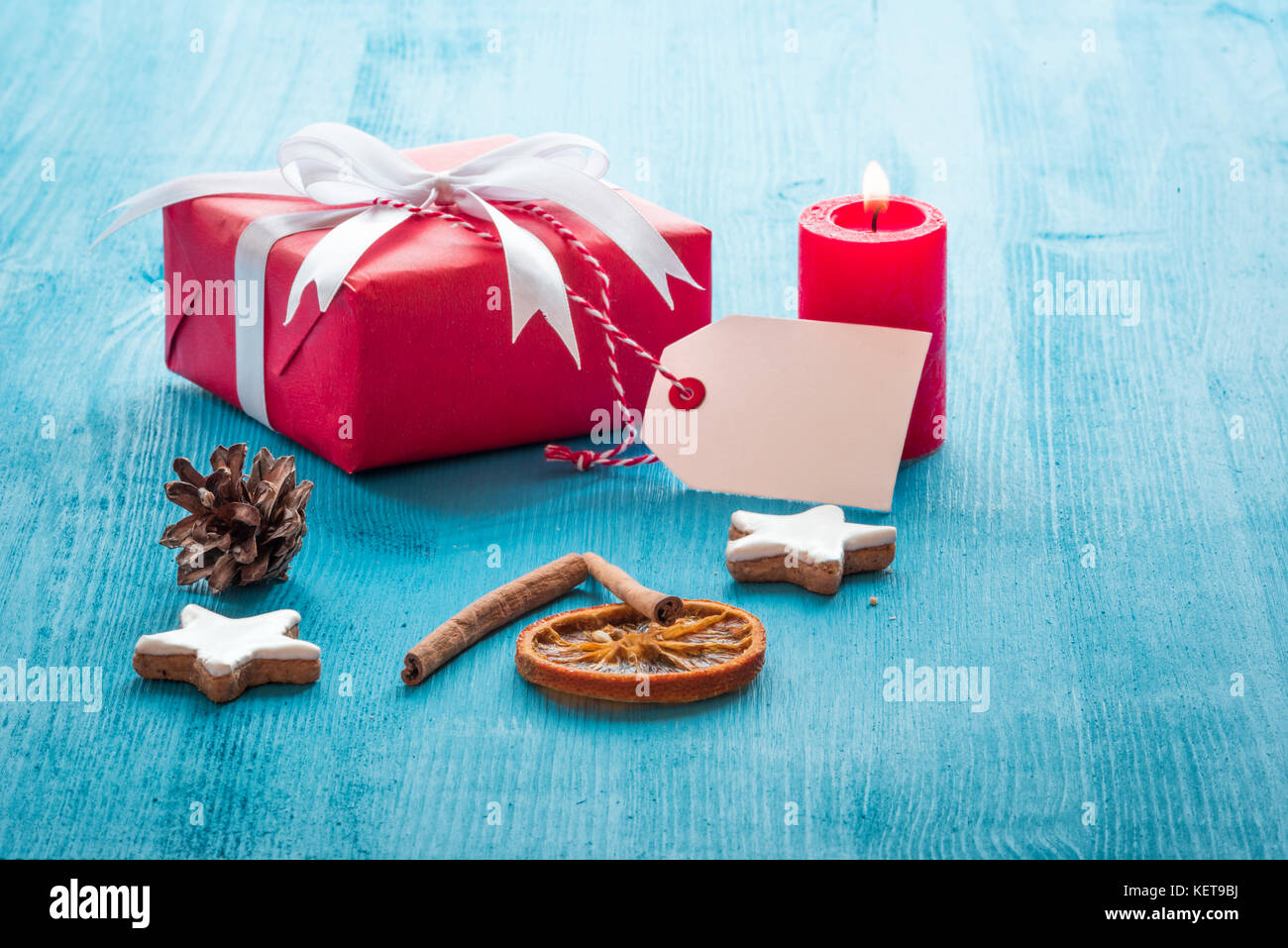 Weihnachten Landschaft mit roter Geschenkbox, eine brennende Kerze, Gingerbread cookies und Zimtstangen auf einem blauen Holztisch Stockfoto