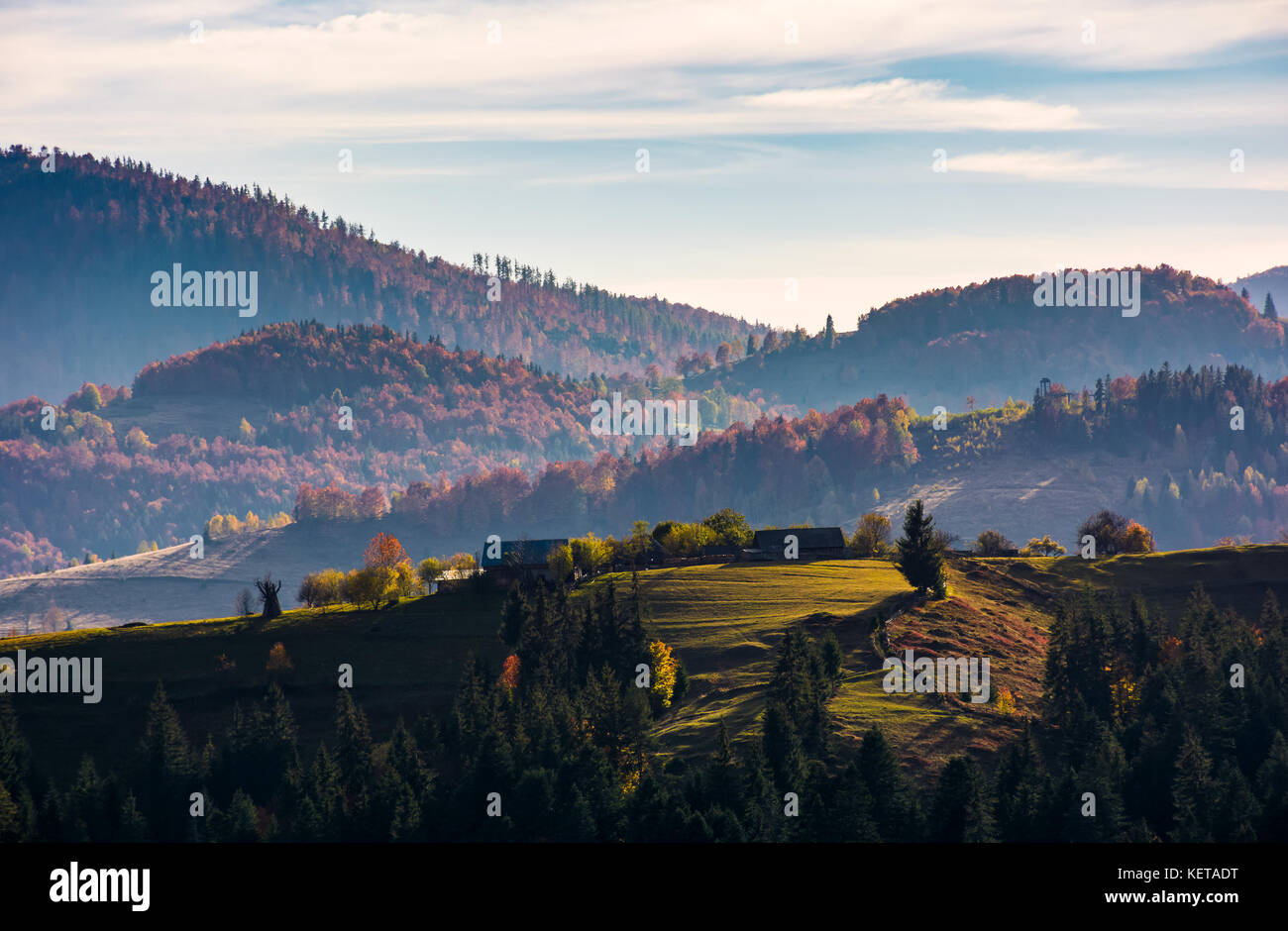Dorf auf einem grasbewachsenen Hügel im Herbst. wunderschönen Sonnenaufgang in den Bergen ländliches Gebiet mit rötlichen Wald Stockfoto