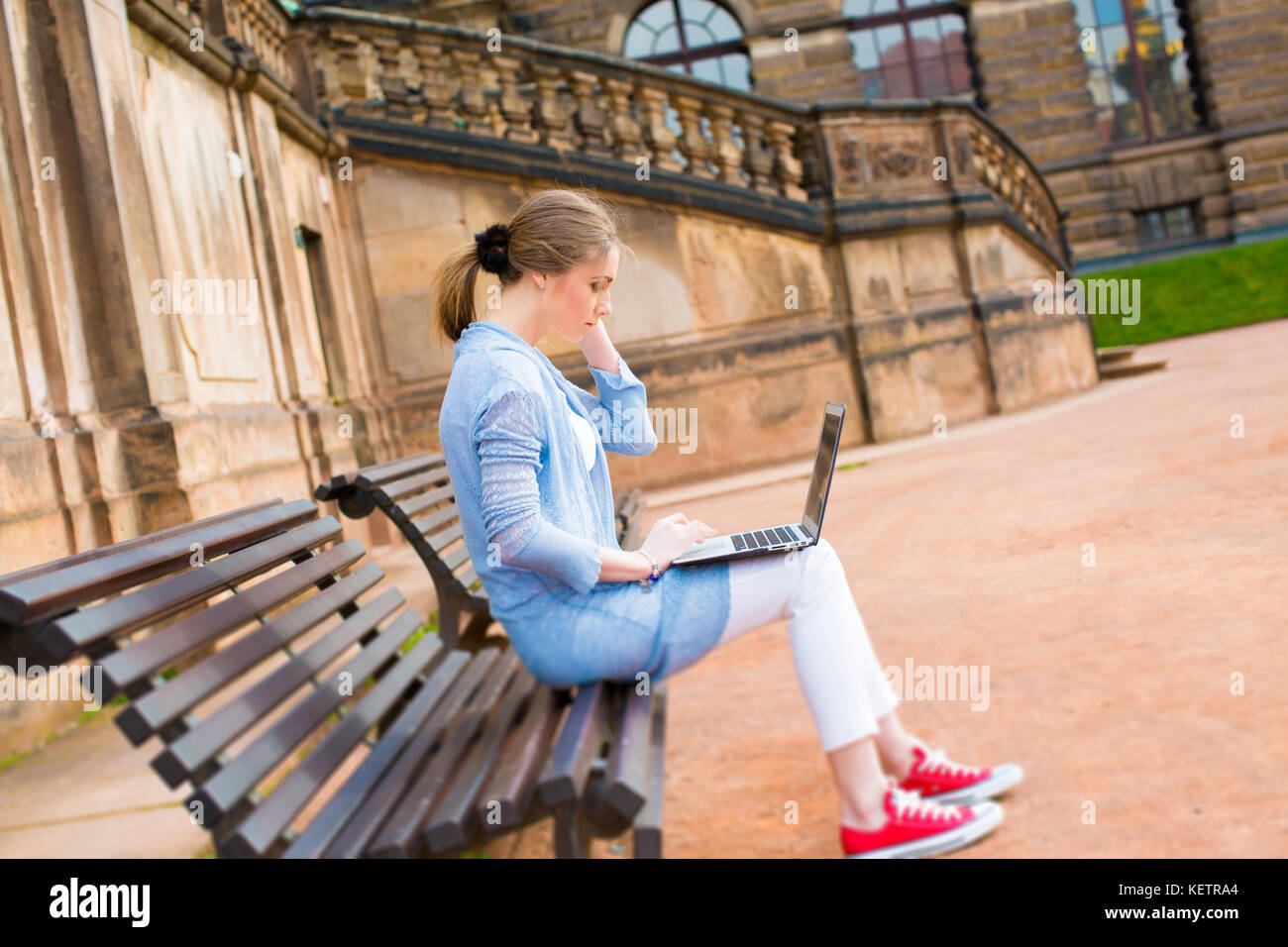 Junge Schülerin mit einem Laptop in einem Park auf einer Bank Stockfoto