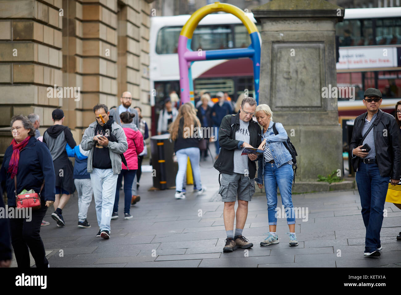 Edinburgh, Schottland, die Royal Mile Canongate verloren Touristen auf einer Karte in der Nähe einer gemalten Security Barrier suchen Stockfoto