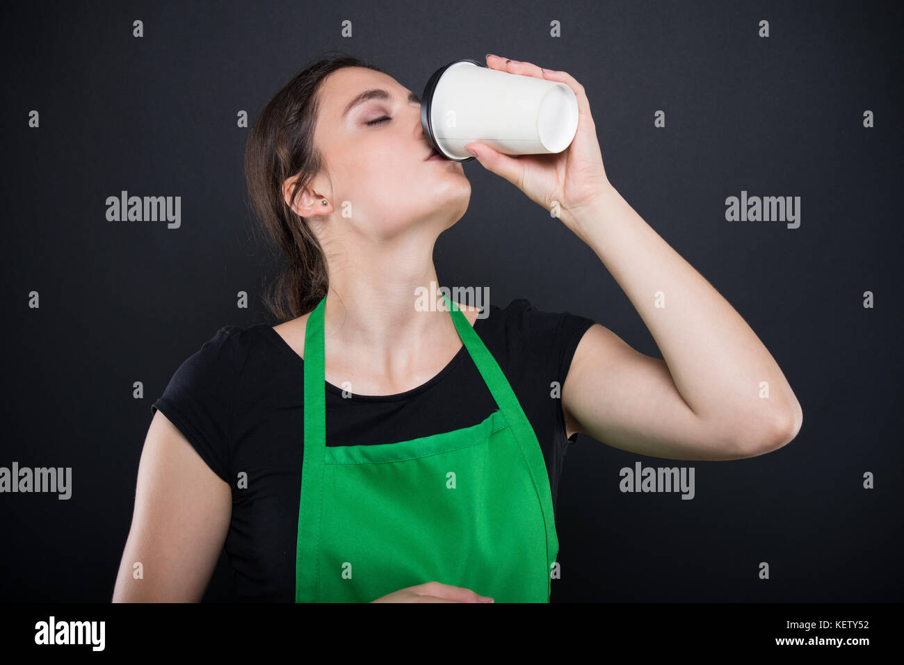 Schöne brünette Verkäufer Verkostung einen frischen Espresso in ihrer Zeit Pause auf dunklem Hintergrund isoliert Stockfoto