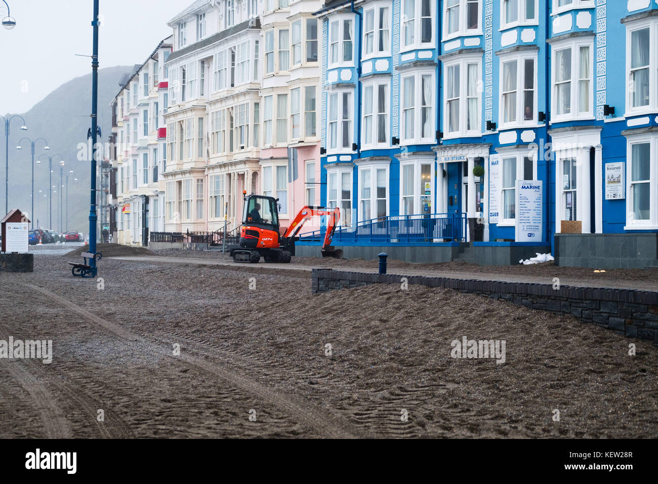 Aberystwyth Wales Vereinigtes Königreich, Montag, 23. Oktober 2017 Vereinigtes Königreich Wetter: Nach dem Sturm Wind und wilde Meere des Sturms Brian, Mitarbeiter des gemeinderats und Auftragnehmer, die JCB's und Bürsten verwenden, beginnen mit der Reinigung der Hunderte Tonnen von Sandsand und Kies, die an der Promenade und am Meer in Aberystwyth an der Küste von Cardigan Bay in westwales angespült wurden. Sie erwarten, dass die Straße bis zum Nachmittag wieder für den Verkehr freigegeben wird. Foto: Keith Morris/Alamy Live News Stockfoto