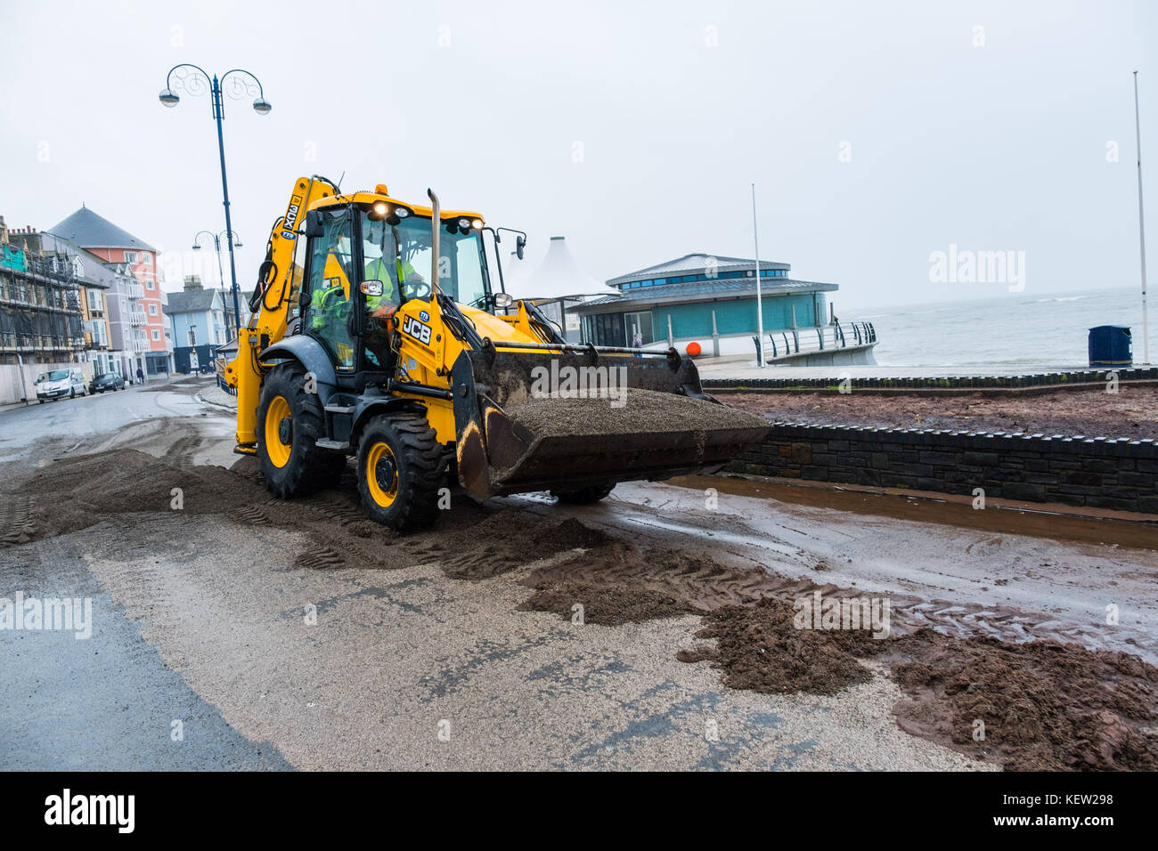 Aberystwyth Wales uk, uk Wetter Montag, 23. Oktober 2017: Nach dem Sturm Winde und wilden Meere der Sturm Brian, lokale Behörde Rat Arbeitnehmer und Auftragnehmer mit Jcb und Bürsten beginnen den Prozess der Clearing die hunderte von Tonnen von Sand und Kies auf die Promenade und das Meer in Aberystwyth gewaschen auf der Cardigan Bay Küste von West Wales. Sie erwarten, dass die Straße für den Verkehr zu haben wieder durch den Nachmittag Foto: Keith Morris/alamy leben Nachrichten Stockfoto