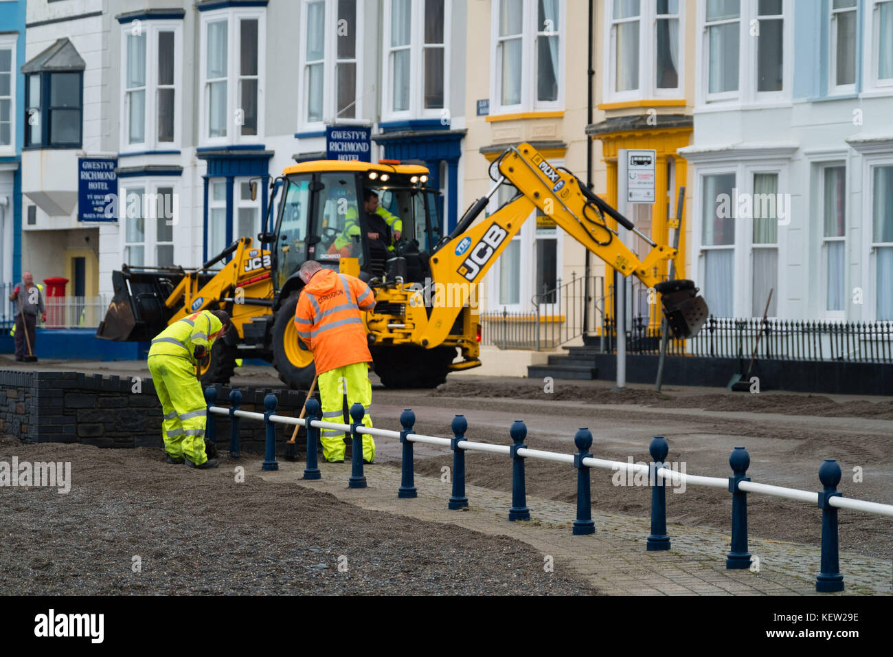 Aberystwyth Wales Vereinigtes Königreich, Montag, 23. Oktober 2017 Vereinigtes Königreich Wetter: Nach dem Sturm Wind und wilde Meere des Sturms Brian, Mitarbeiter des gemeinderats und Auftragnehmer, die JCB's und Bürsten verwenden, beginnen mit der Reinigung der Hunderte Tonnen von Sandsand und Kies, die an der Promenade und am Meer in Aberystwyth an der Küste von Cardigan Bay in westwales angespült wurden. Sie erwarten, dass die Straße bis zum Nachmittag wieder für den Verkehr freigegeben wird. Foto: Keith Morris/Alamy Live News Stockfoto