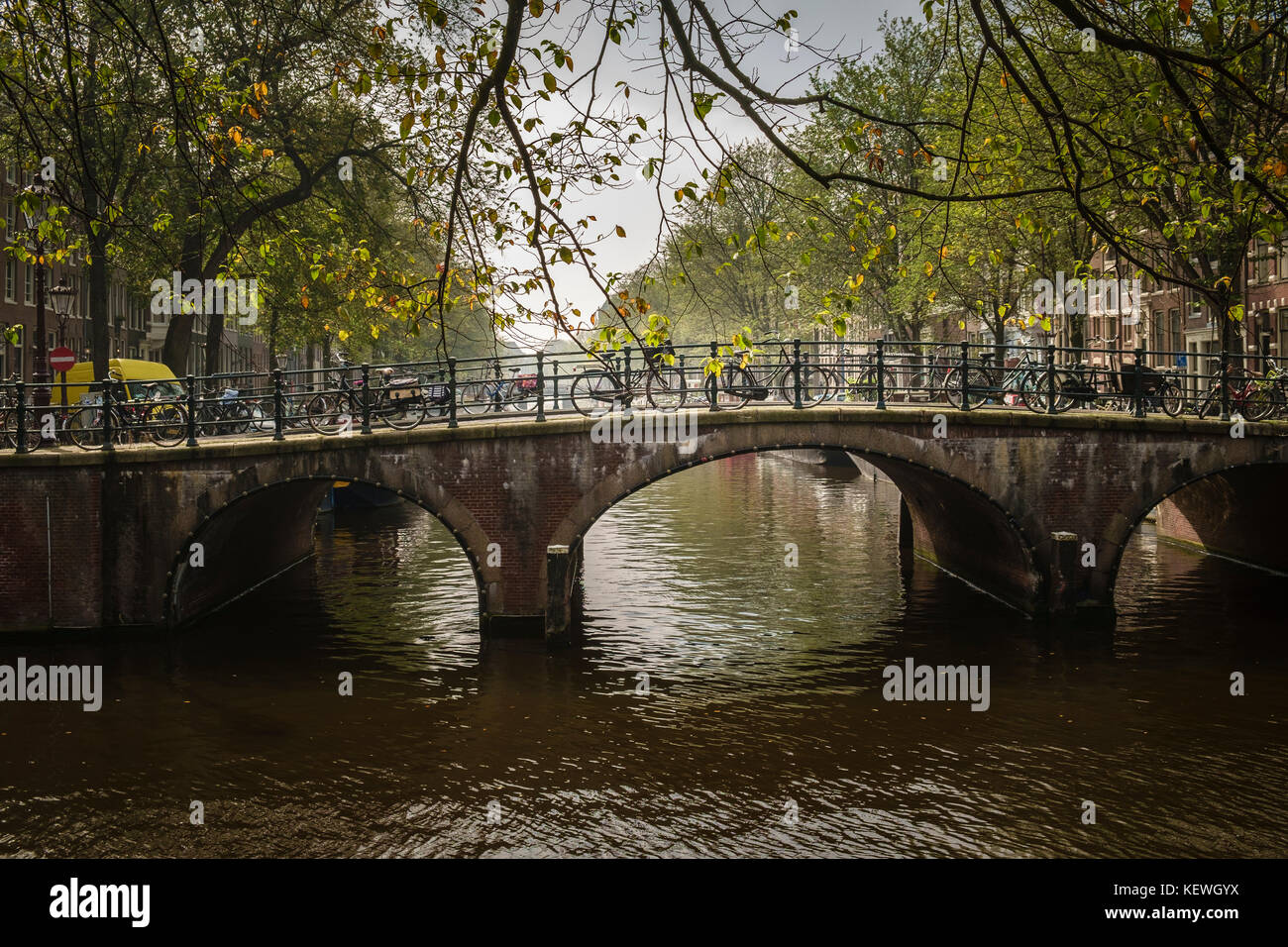 Herbst fällt Licht auf Fahrrädern auf einer Brücke über einem Amsterdam Canal geparkt. Stockfoto