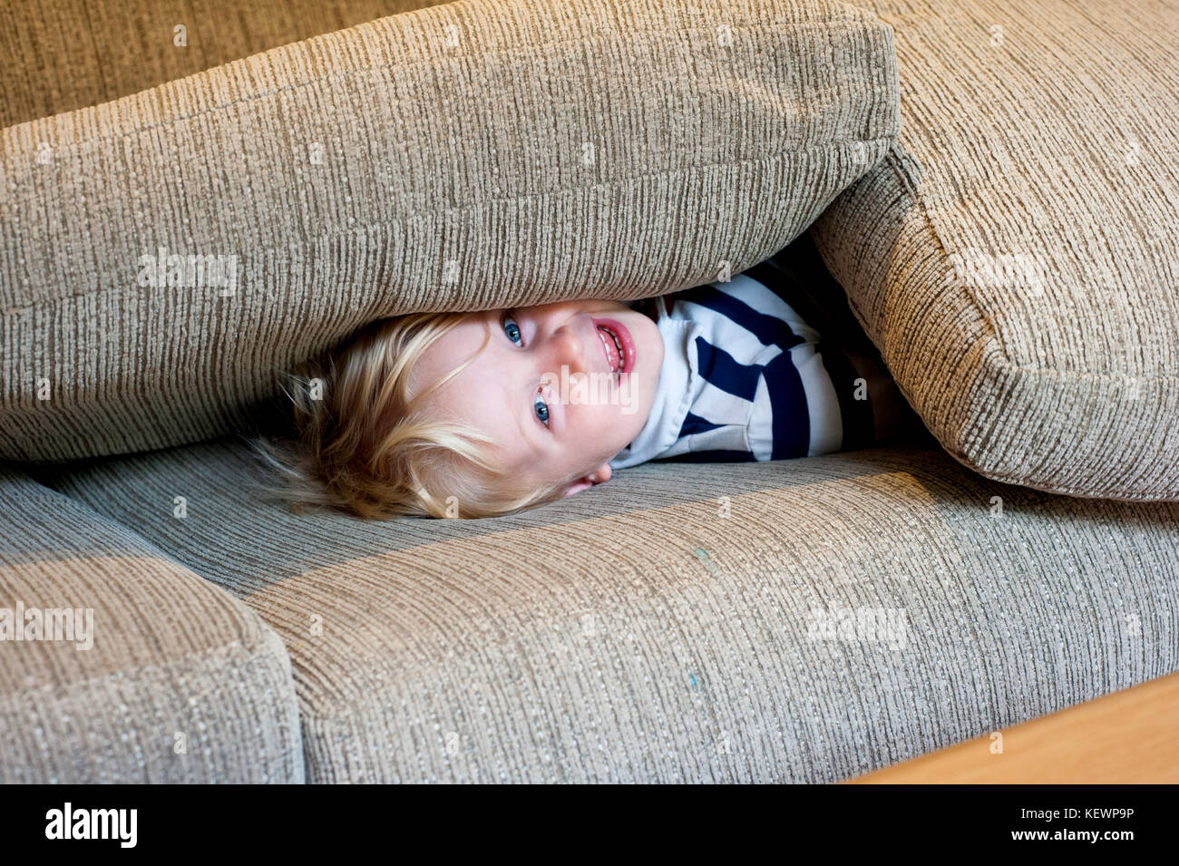 Kleiner Junge versteckt sich unter Sofakissen Stockfoto