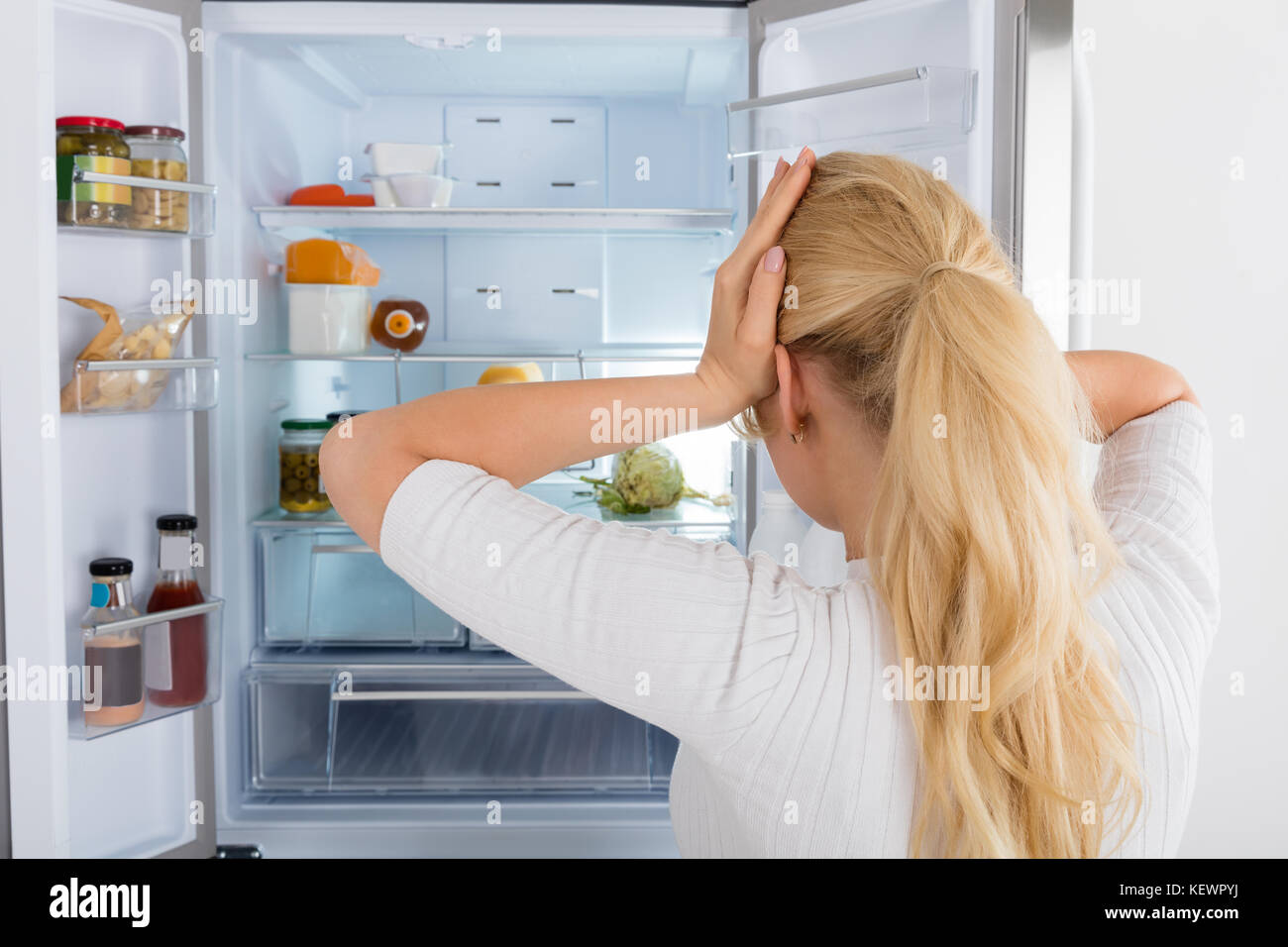 Rückansicht eines verwirrten Frau in den Kühlschrank schauen, Stockfoto