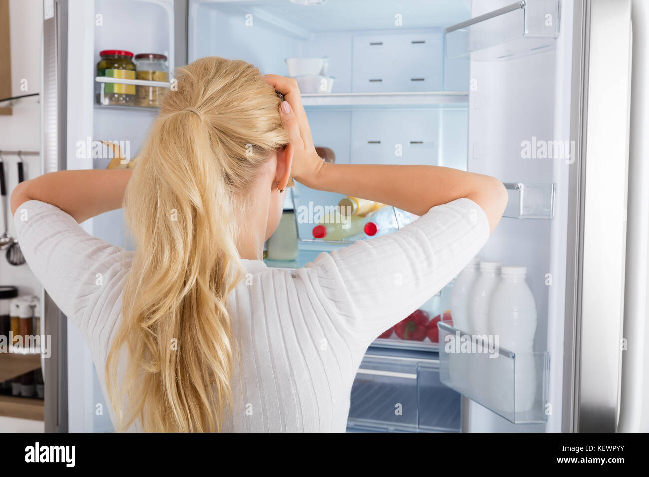 Rückansicht eines verwirrten Frau in den Kühlschrank schauen, Stockfoto