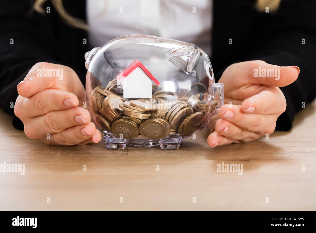 Geschäftsfrau schützt ihre Ersparnisse mit Hausmodell in Einer Sparkasse. Investitionskonzept Für Immobilien Stockfoto