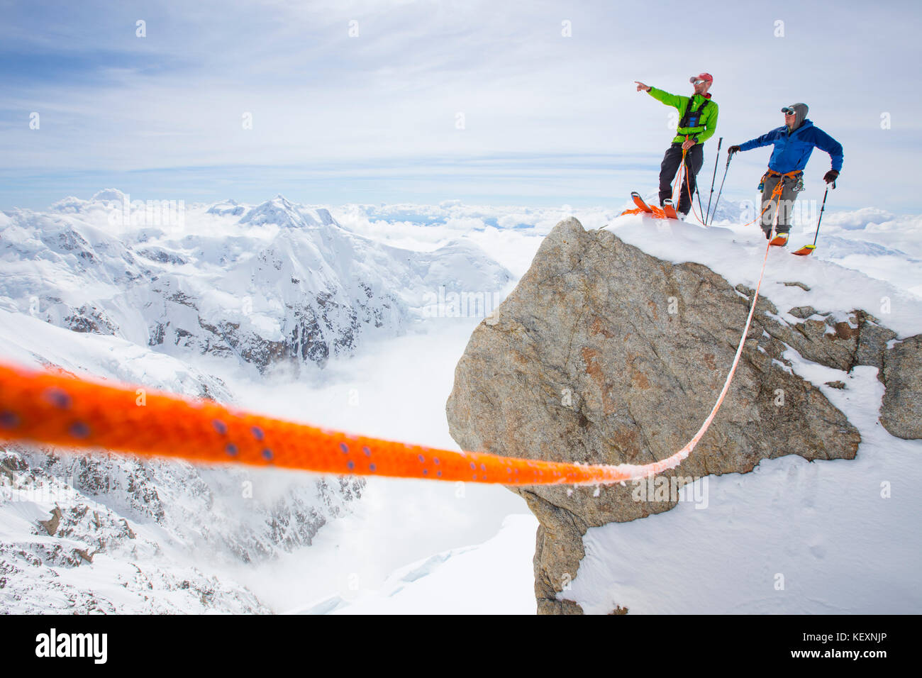 Zwei Skibergsteiger stehen auf einem Gipfel im Denali Nationalpark. Einer weist den Weg zu seinem Kumpel. Ein Sicherheitsseil verbindet das Duo. Denali, mit seinen vielen Gletschern und viel Schnee fallen im Sommer ist ein perfekter Berg für Backcountry Skitouren, Alpinismus und Freeriden. Stockfoto