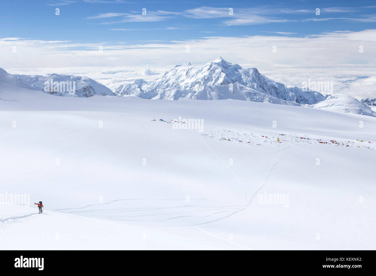 Ein Skibergsteiger auf seinem Weg auf Denali in Alaska, mit 14.000 Fuß Lager im Hintergrund sichtbar. Stockfoto