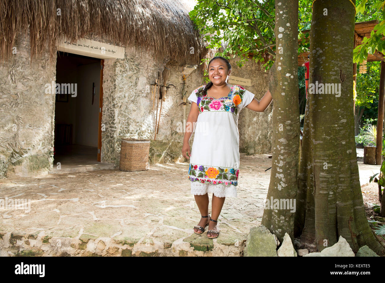 Junge lächelnde Frau in traditioneller Kleidung steht am Baum in der Nähe der Stadt Coba in Quintana Roo, Mexiko Stockfoto
