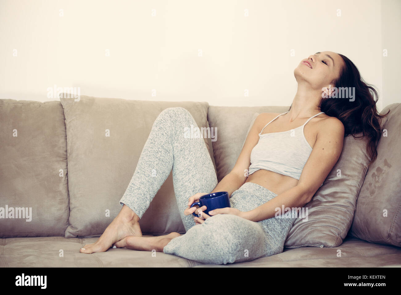 Junge hübsche asiatische Frau sitzt auf der Couch entspannt lächelnden Gesicht Ausdruck blau Tasse in den Händen Stockfoto