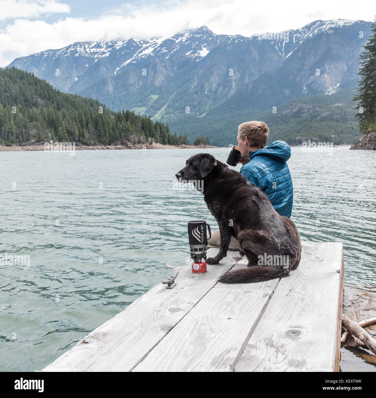 Ein Mann und sein Hund auf einem Dock auf Ross See in North Cascades National Park sitzen. Stockfoto