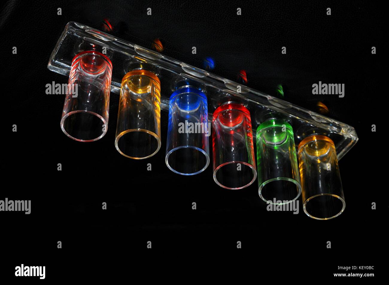 'Shine and Reflect' Shot-Glas, das auf künstlerische Weise angeordnet ist und einen einzigartigen, farbenfrohen Effekt von Licht und Reflexion im schwarzen Hintergrund erzeugt. Stockfoto