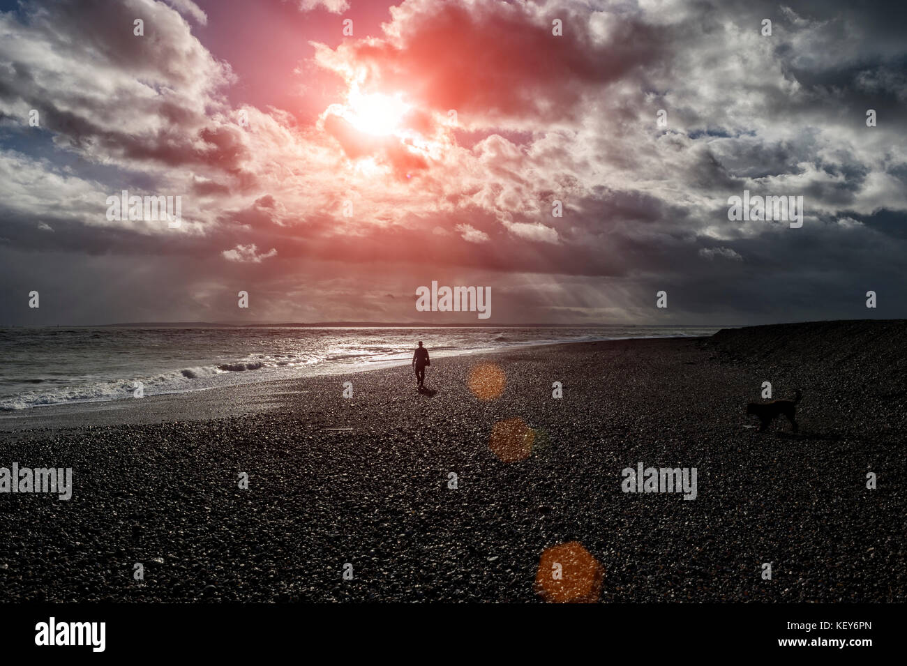 Mann in Silhouette entlang ein Kiesstrand mit dramatischen Himmel Stockfoto