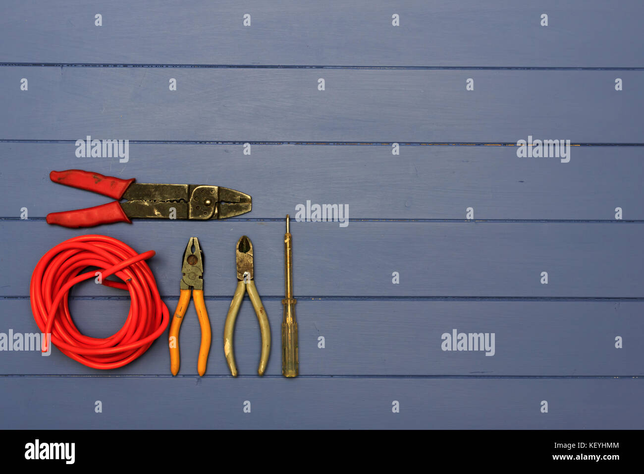 Zange, Schere, kleine elektrische Prüfung Schraubendreher, paar Abisolierzangen und Rolle der roten Kabel auf einem blauen Hintergrund schäbig Board Stockfoto