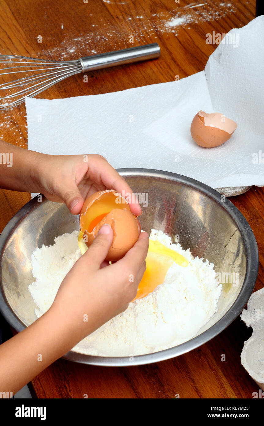 Kind kochen Pfannkuchen, Hände Aufschlagen der Eier, Milch und Mehl in eine Schüssel auf dem Tisch Stockfoto