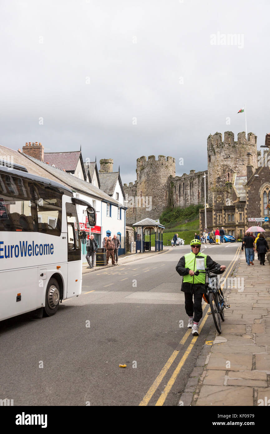 Radfahrer drücken Elektrofahrrad, Conwy Stadt High Street mit Schloss im Hintergrund Stockfoto