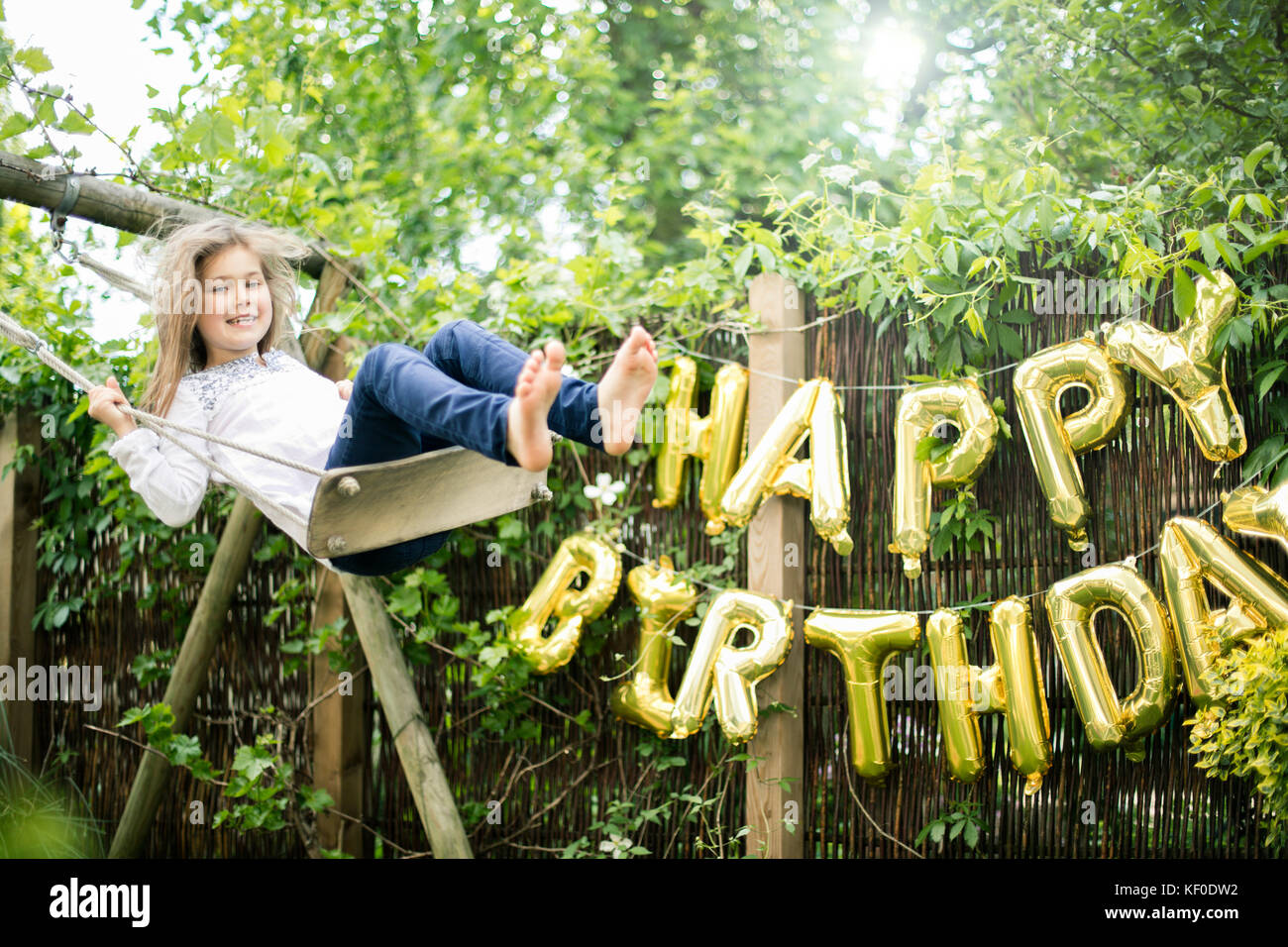 Portrait von swingenden Mädchen im Garten mit Dekoration für Geburtstagsfeier im Hintergrund Stockfoto