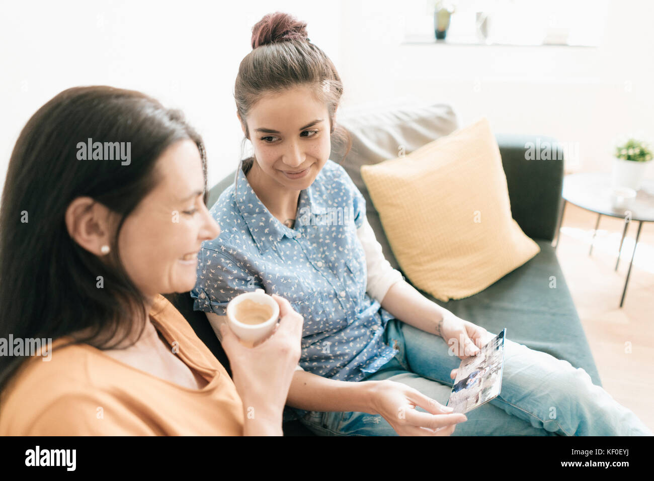 Mutter und erwachsene Tochter sitzen auf der Couch zu Hause Betrachten von Fotos Stockfoto
