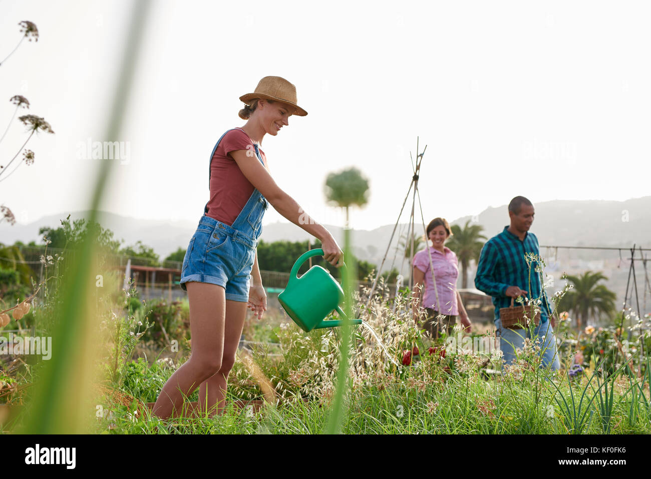 Lächelnden jungen Landwirt mit Gießkanne und Freunde im Hintergrund Stockfoto