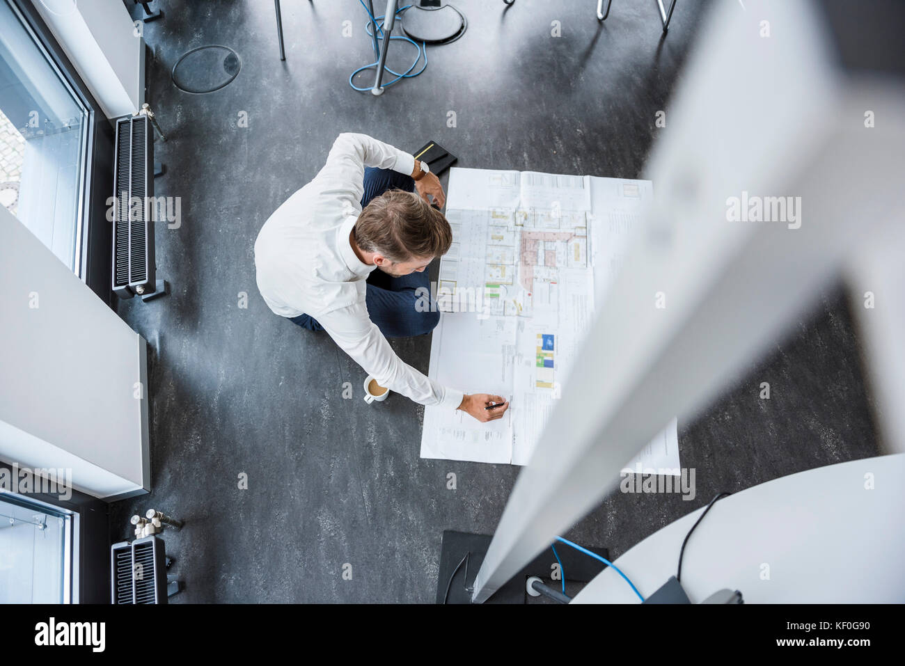 Unternehmer sitzen auf dem Fußboden seines Büros am Bau Plan arbeiten, Ansicht von oben Stockfoto