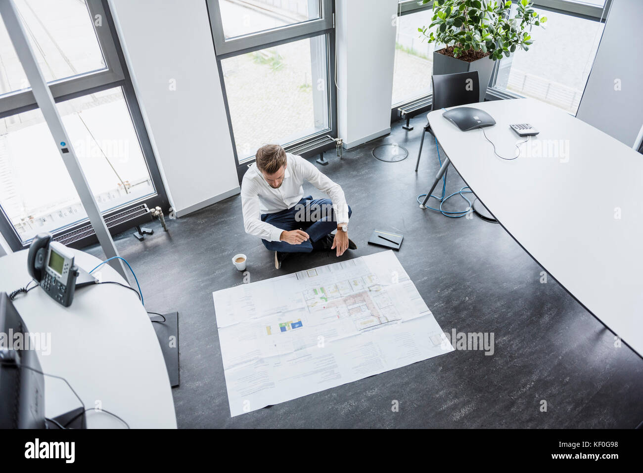 Unternehmer sitzen auf dem Fußboden seines Büros am Bau Plan suchen Stockfoto