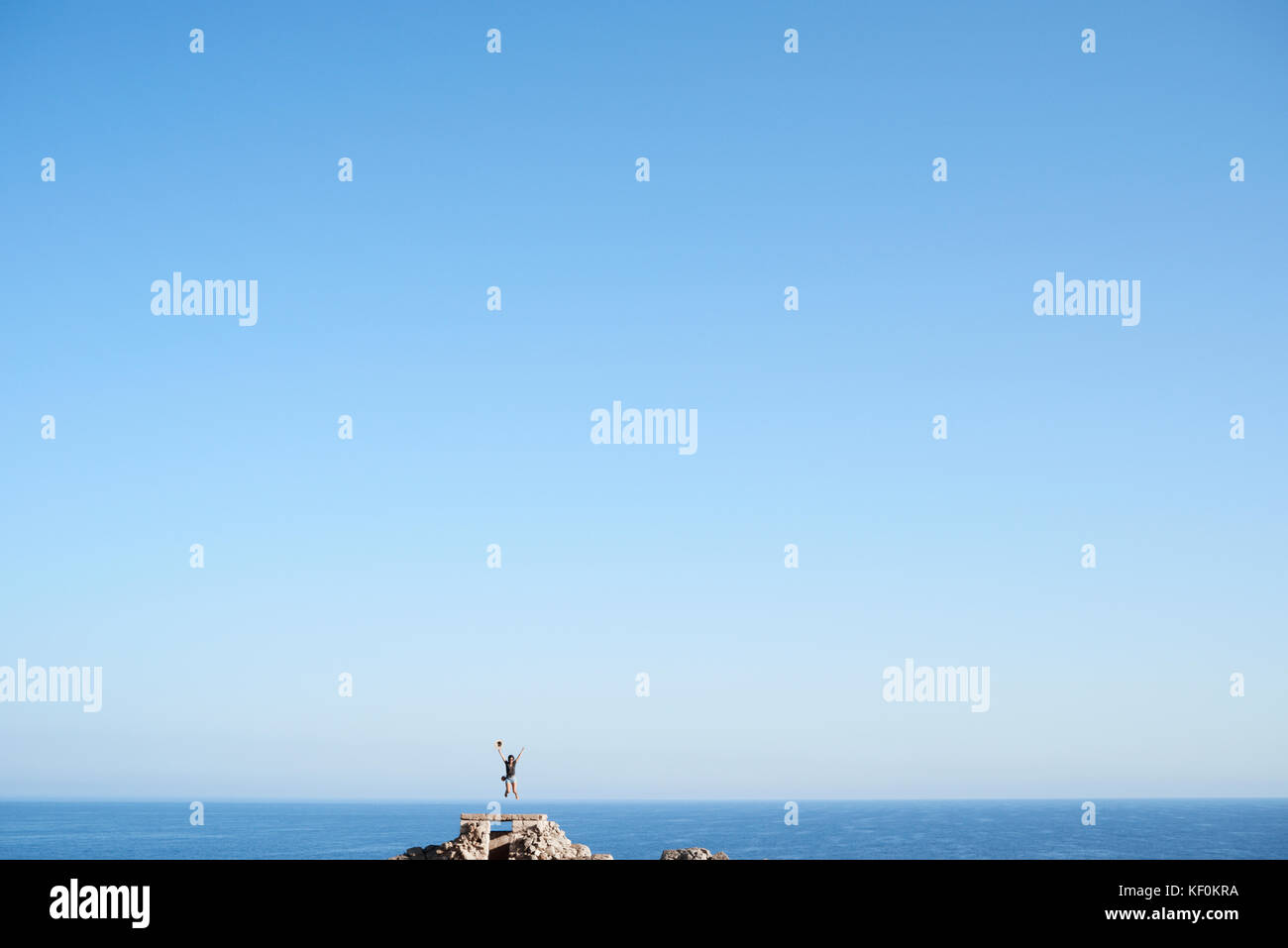 Menorca, Spanien, Alleinreisende gegen Sea Horizon Holding einen Hut in der Insel Menorca springen, Alleinreisende Stockfoto