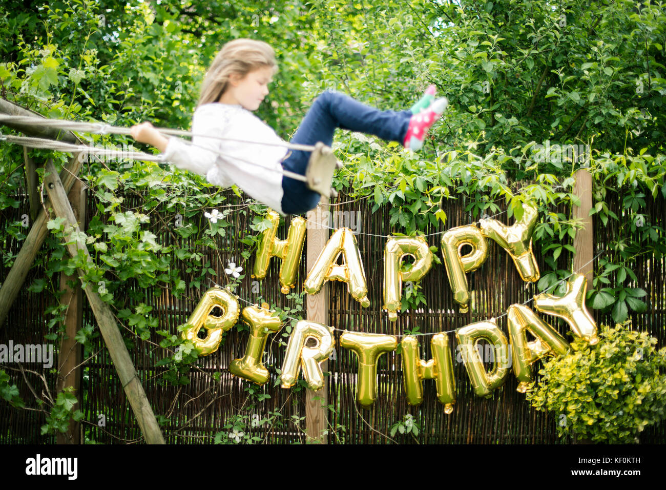 Dekoration für Geburtstagsfeier im Garten mit goldenen Luftballons und schwungvollen Mädchen im Vordergrund Stockfoto