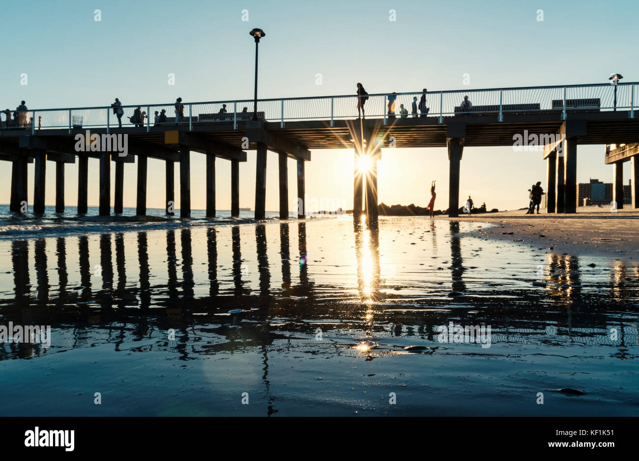 Silhouette Menschen auf und unter dem Brighton Beach Pier auf Coney Island mit Sunburst Stockfoto