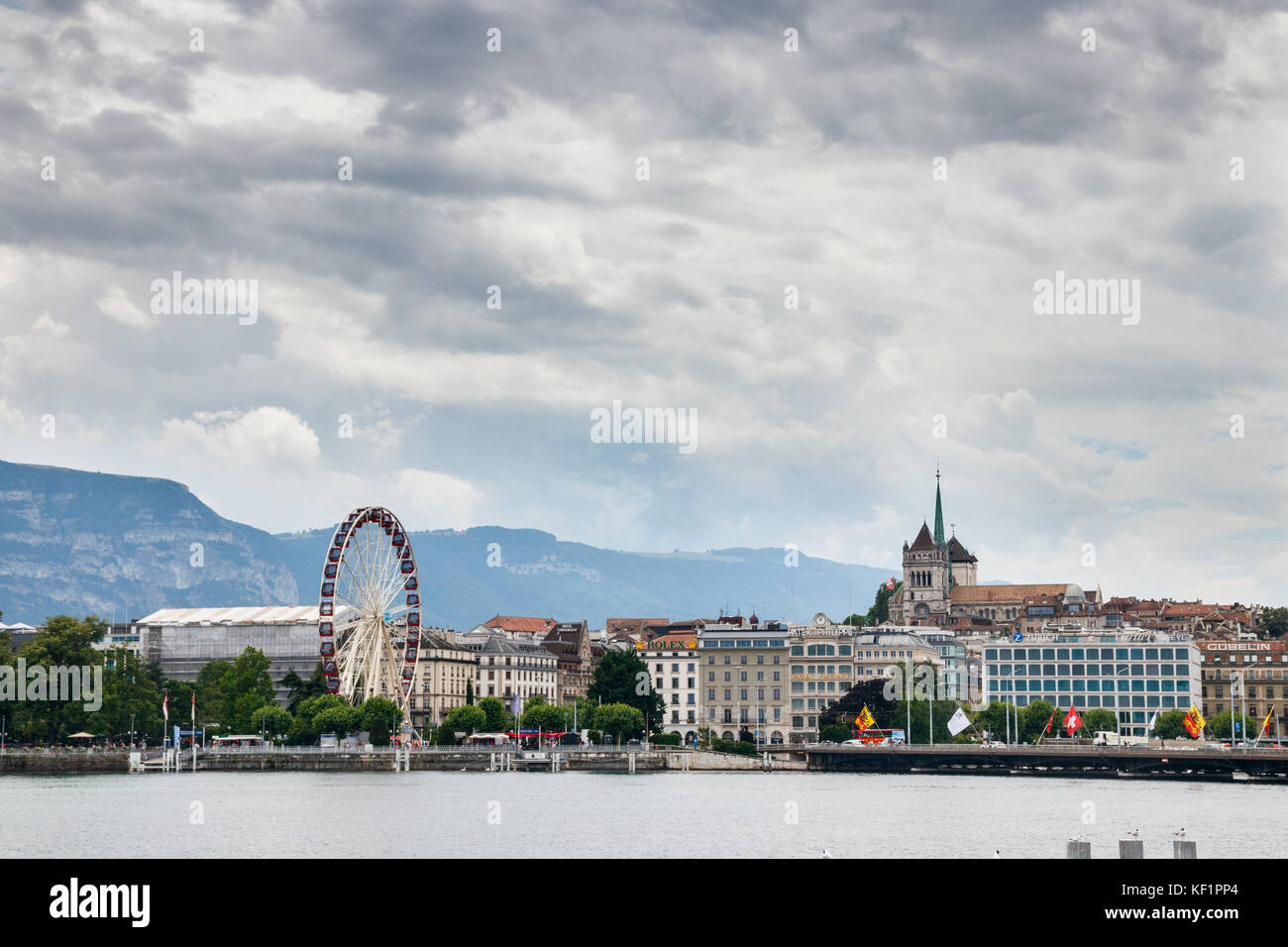Blick auf die Rhône und die Altstadt mit der Kathedrale St. Peter und ein Riesenrad am Ufer unter einem bewölkten Himmel. Genf, Schweiz. Stockfoto
