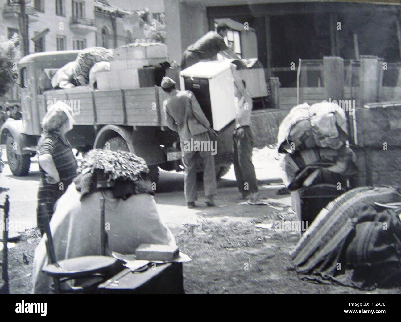 Ein historisches Bild, das die Evakuierung von Familien darstellt, wahrscheinlich während einer Zeit des Konflikts oder Umbruchs. Das Foto erfasst die emotionale und chaotische Natur von Familienevakuierungen während einer Kriegs- oder Vertreibungszeit. Stockfoto