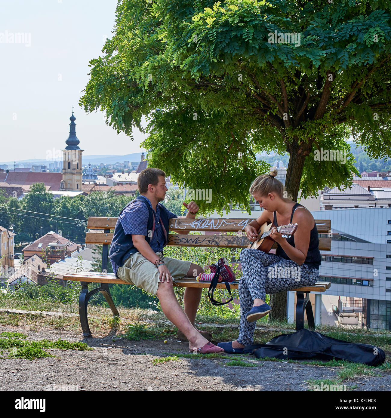 Paar sitzt auf einer Holzbank mit Blick auf die Stadt Cluj, die Frau, die in der Wiedergabe einer Gitarre und Gesang Stockfoto