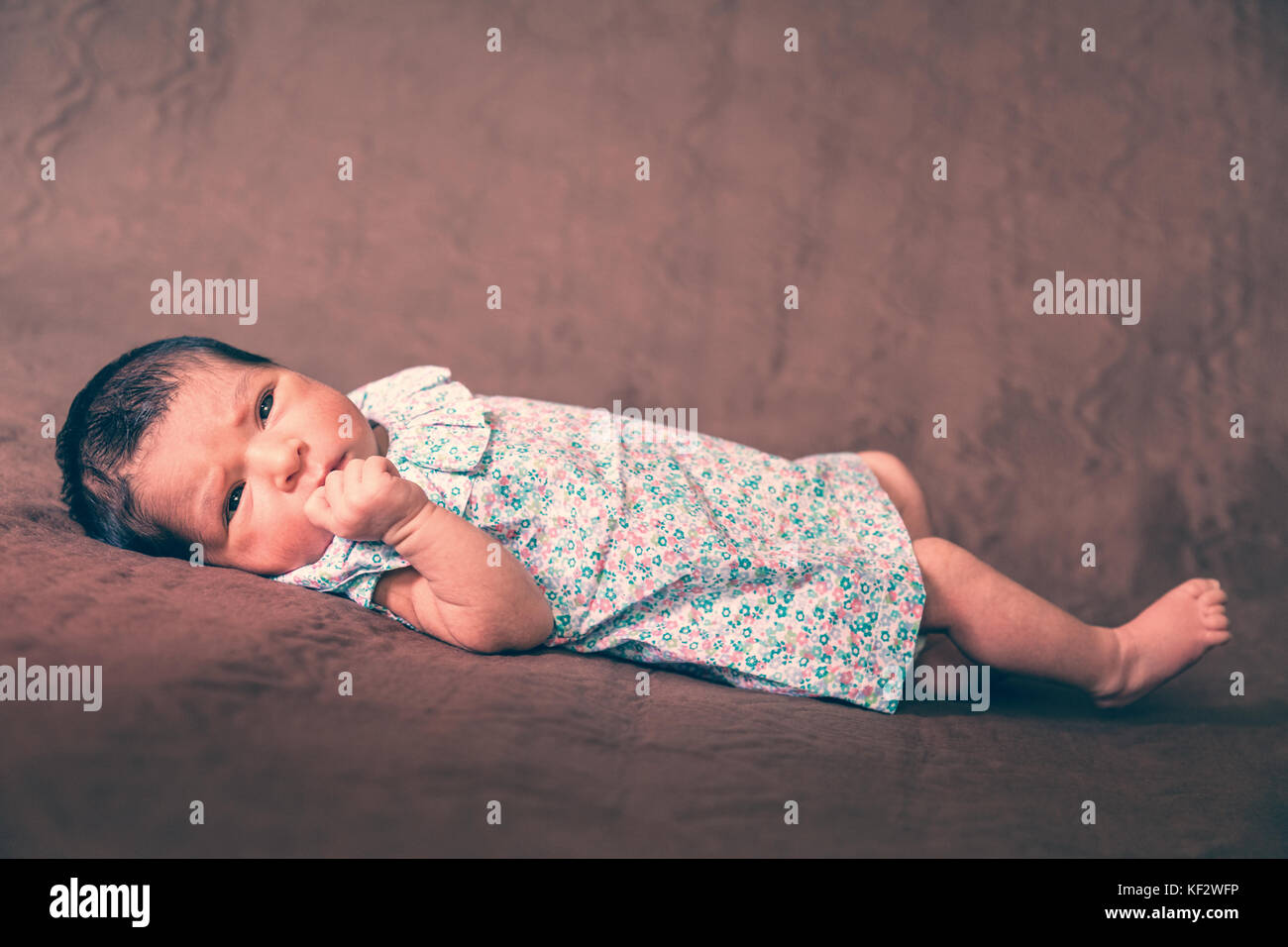 Cute zwei Wochen alte Neugeborene Mädchen hinlegen, die Augen öffnen und Suchen rund um das Tragen eines geblümten Kleid/neugeborenen Baby girl liegend Bett Kind Augen Stockfoto