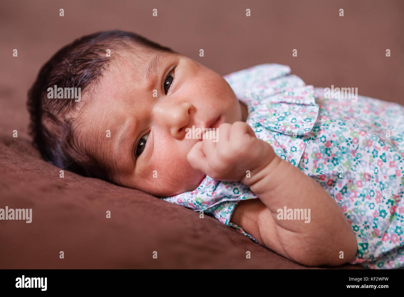 Nahaufnahme, Porträt einer niedlichen Zwei Wochen alte Neugeborene Mädchen hinlegen, die Augen öffnen und Suchen rund um das Tragen eines geblümten Kleid/neugeborenen Baby girl Stockfoto