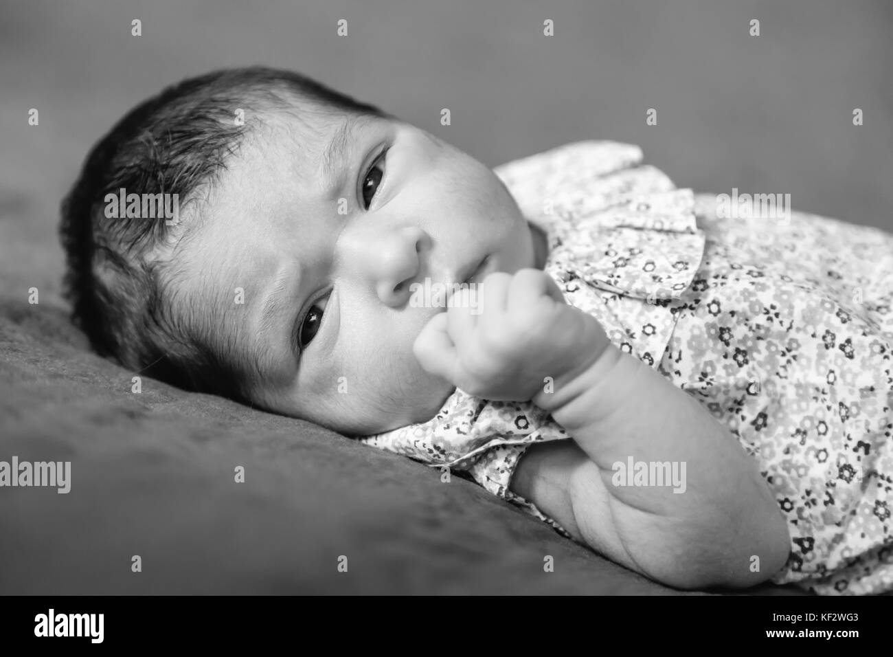 Nahaufnahme, Porträt einer niedlichen Zwei Wochen alte Neugeborene Mädchen hinlegen, die Augen öffnen und Suchen rund um das Tragen eines geblümten Kleid/neugeborenen Baby girl Stockfoto