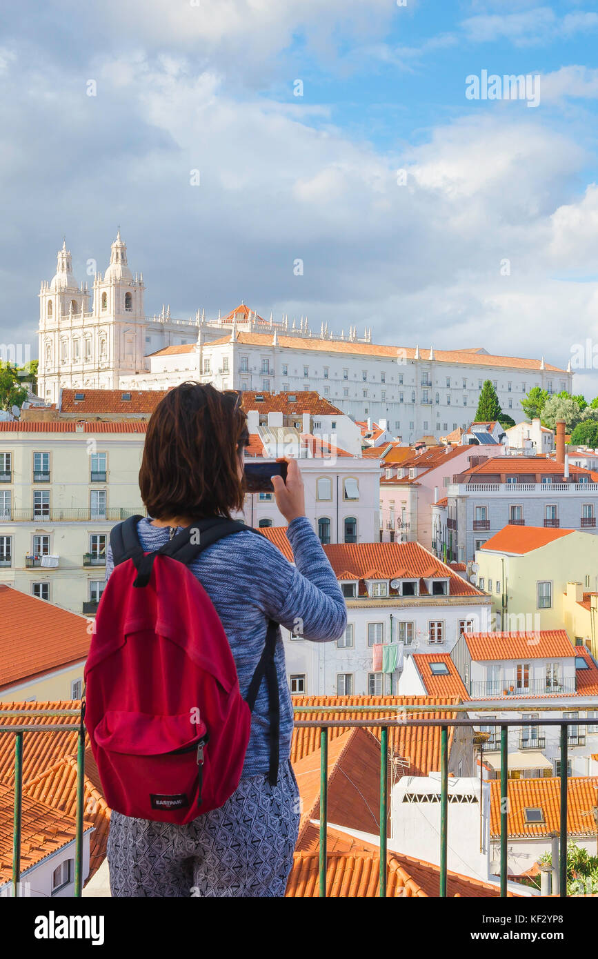 Junge Frau reist, Rückansicht einer alleinreisende Frau in einem roten Rucksack, die ein Foto von Gebäuden im Alfama-Viertel von Lissabon, Portugal, macht. Stockfoto