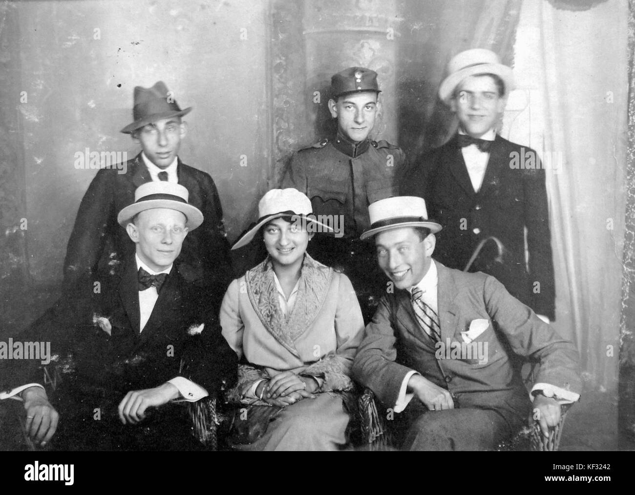 Ein Tableau mit einer Frau und Männern in modischer Kleidung, mit Hut, Uniform, Gehstock und Korbstuhl, aufgenommen in einem Studio mit Mode und Stil des 20. Jahrhunderts. Stockfoto