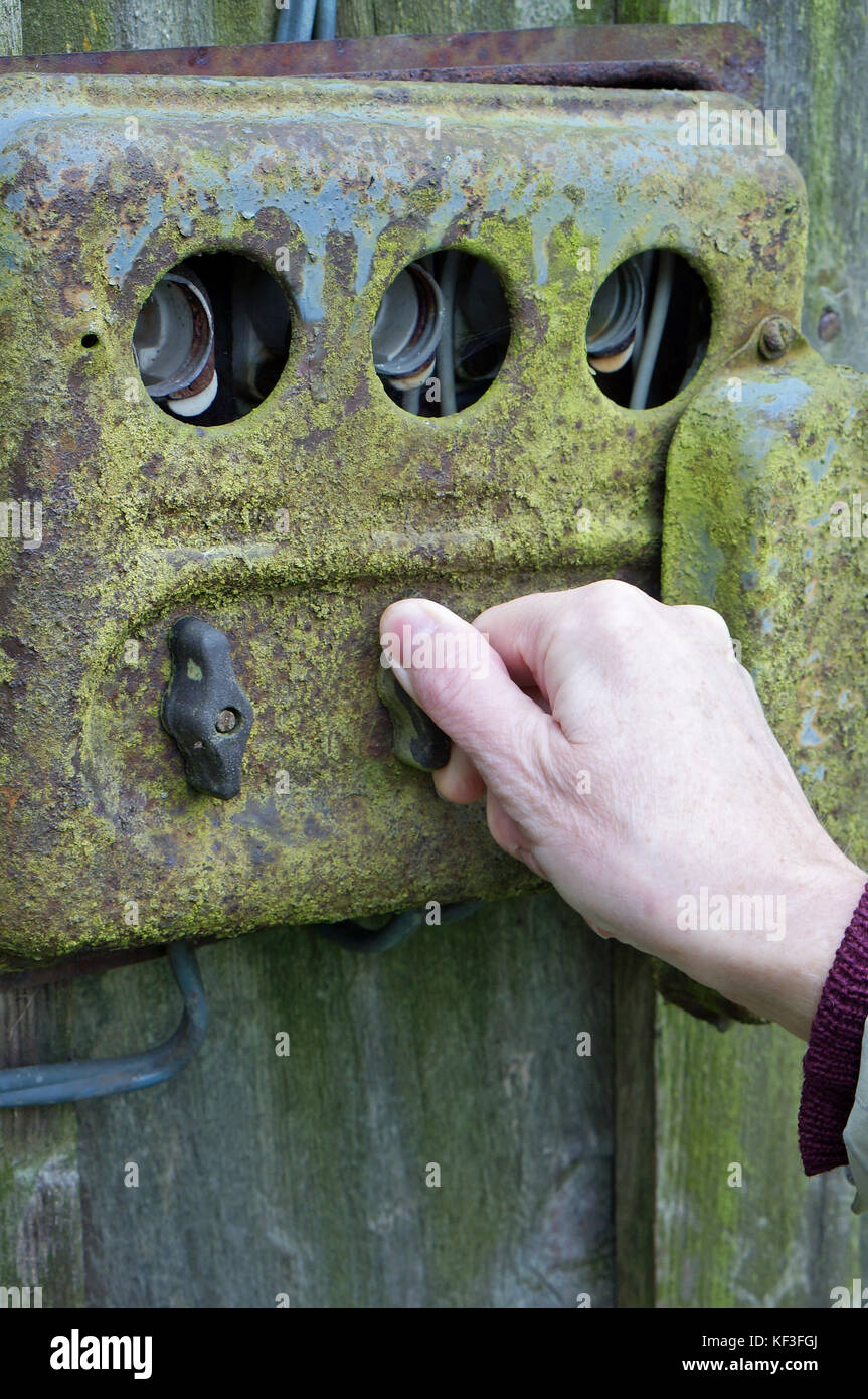 Die Hand einer älteren Frau schaltet Elektrizität an einer alten rostigen ländlichen Schalttafel. Concept Outdoor-Foto zum Herbsttag Stockfoto