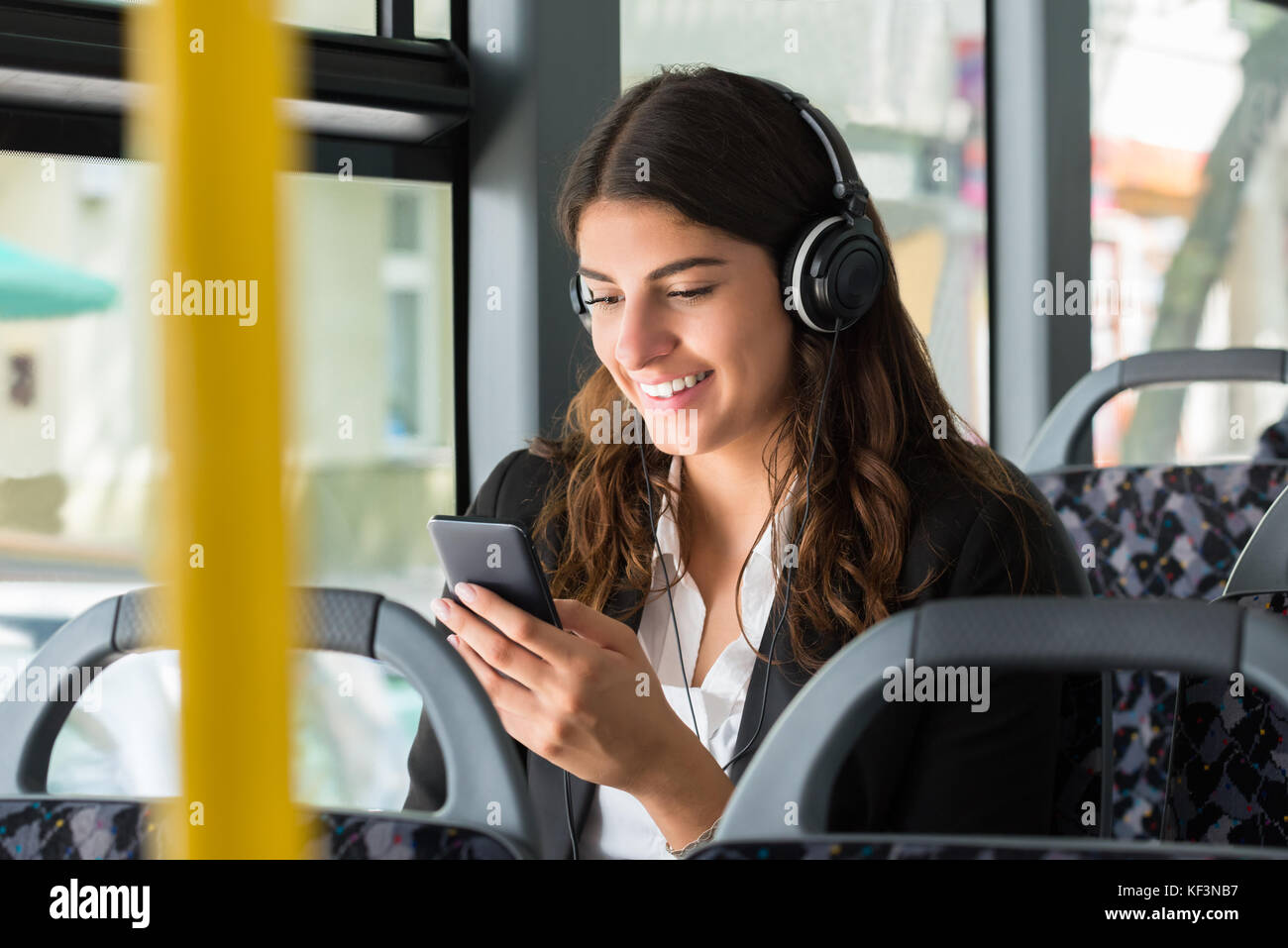 Lächelnden jungen Geschäftsfrau mit Handy Musik hören, während Sie mit dem Bus reisen Stockfoto