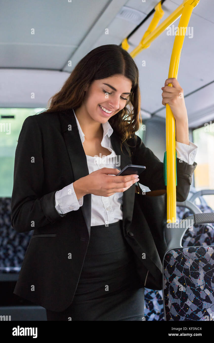 Junge lächelnde Geschäftsfrau mit Smartphone während Reisen mit öffentlichen Verkehrsmitteln Stockfoto