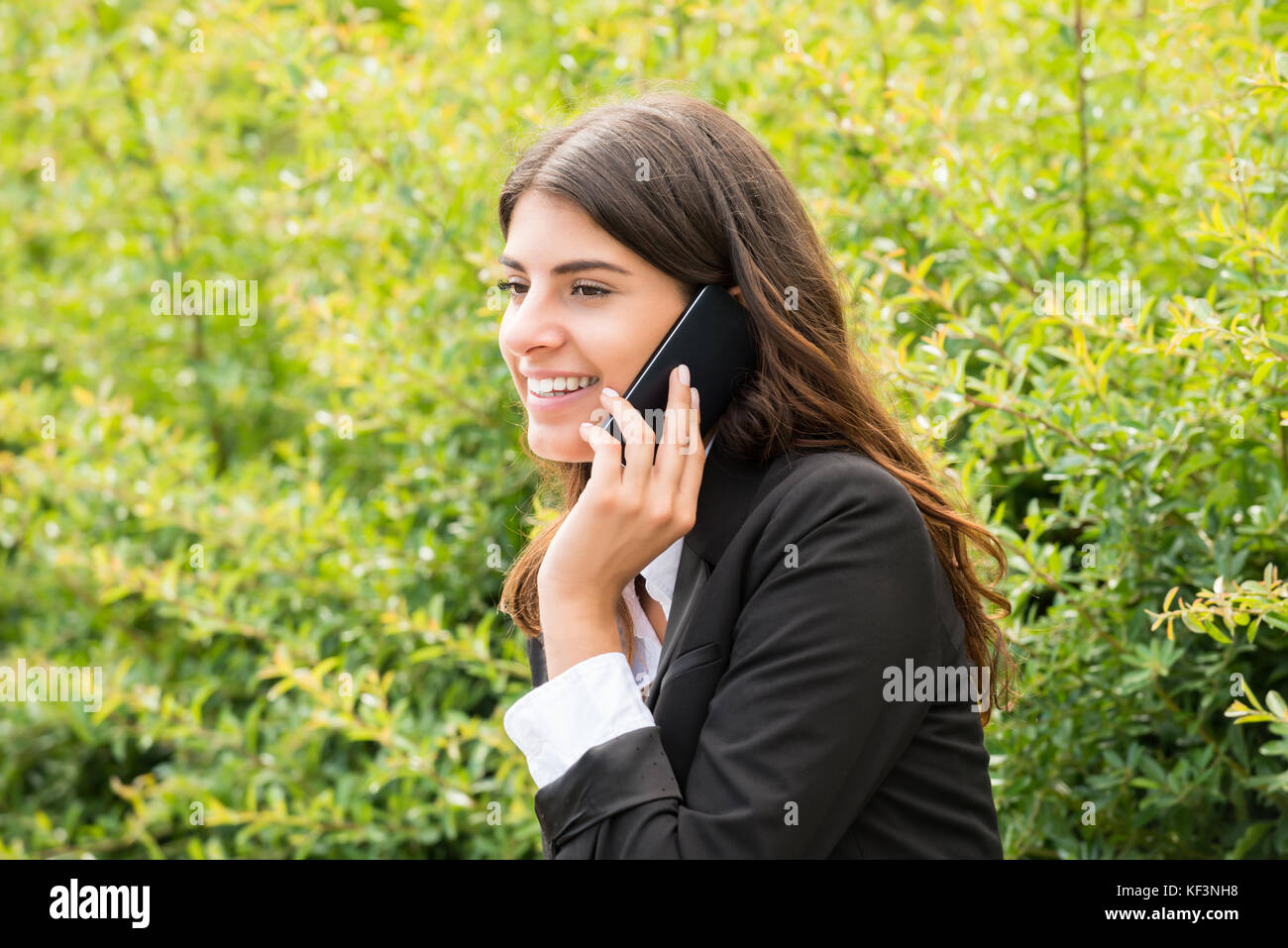 Glückliche junge geschäftsfrau sitzt auf der bank Gespräch am Handy im Park Stockfoto