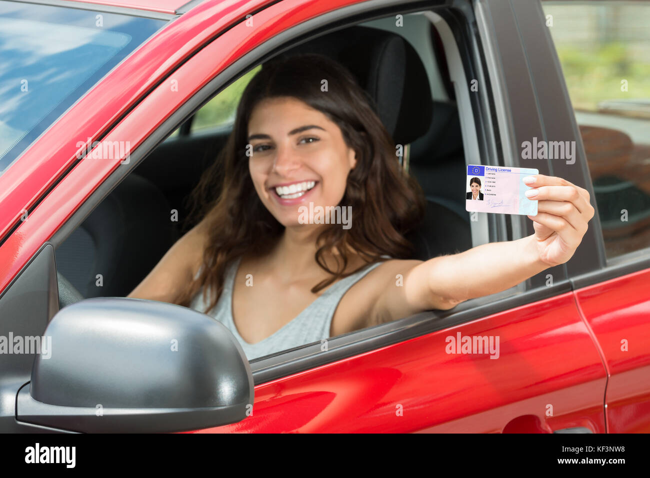 Lächelnde junge Frau ihren Führerschein Übersicht aus dem offenen Autofenster Stockfoto