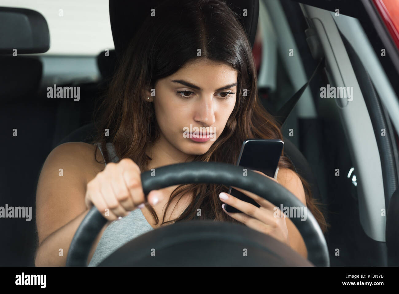 Junge Frau von ihrem Mobiltelefon auf der Suche beim Sitzen im Auto Stockfoto