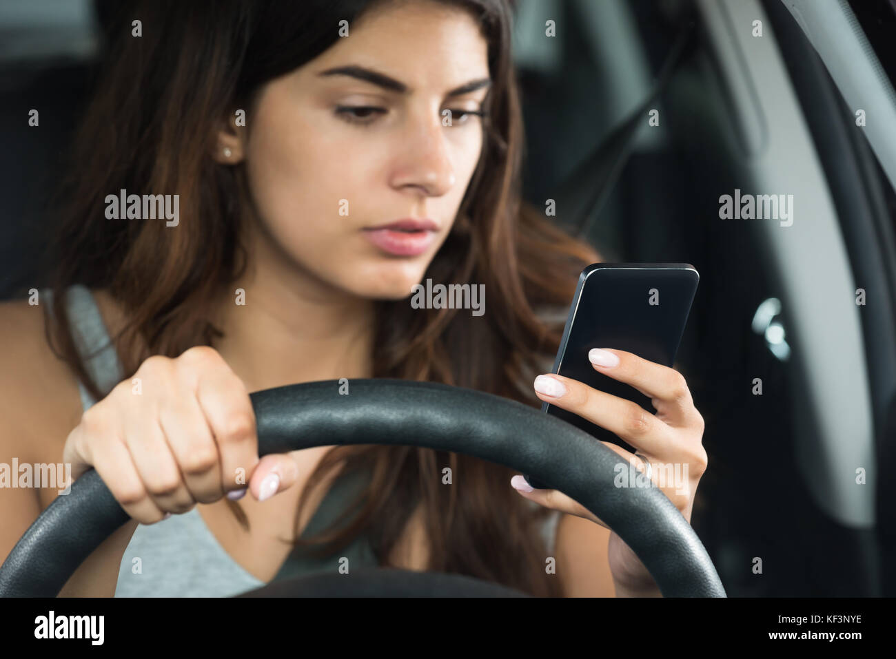 Junge Frau von ihrem Mobiltelefon auf der Suche beim Sitzen im Auto Stockfoto