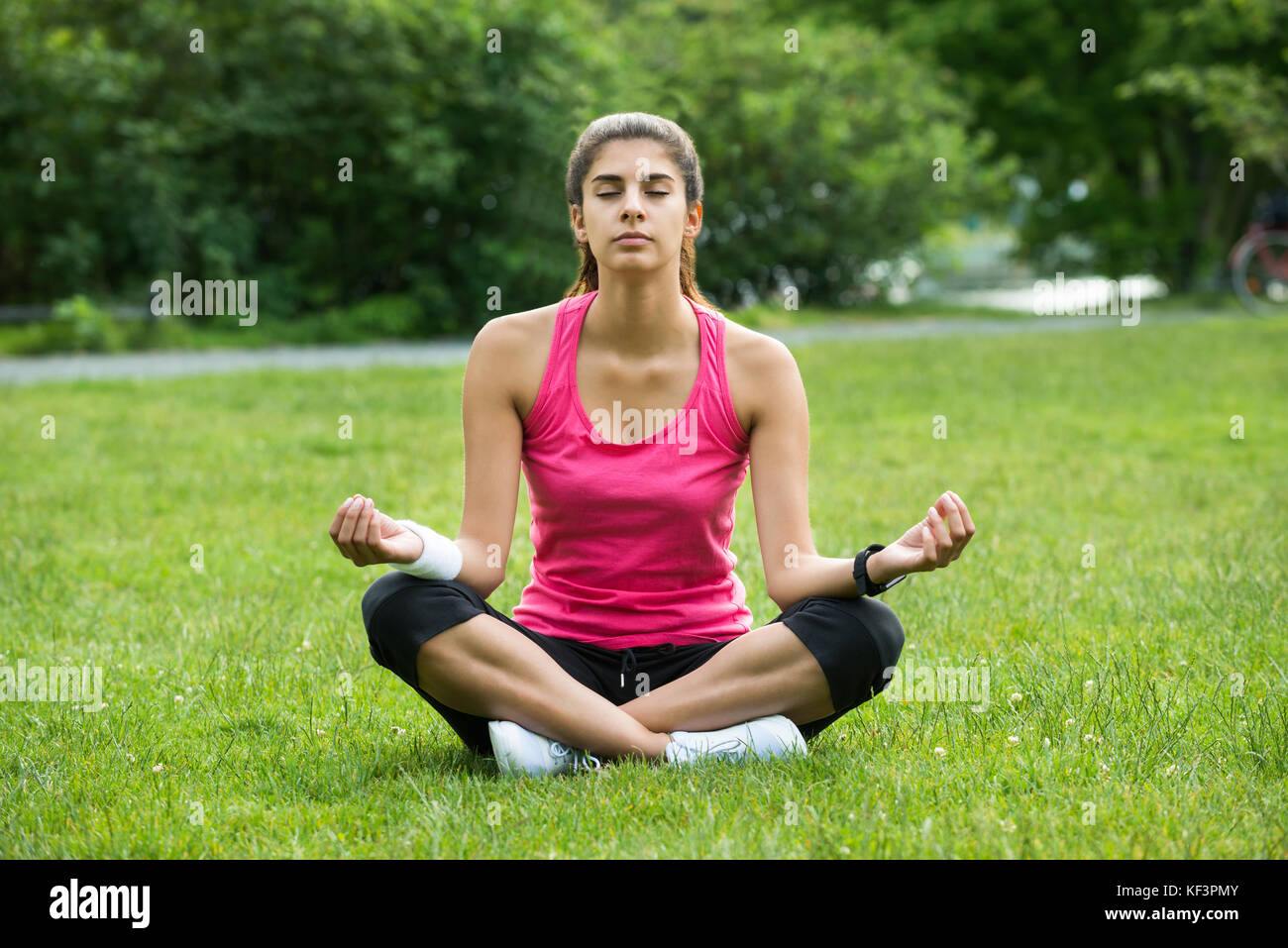 Junge Frau sitzt auf Gras Meditation in Park Stockfoto